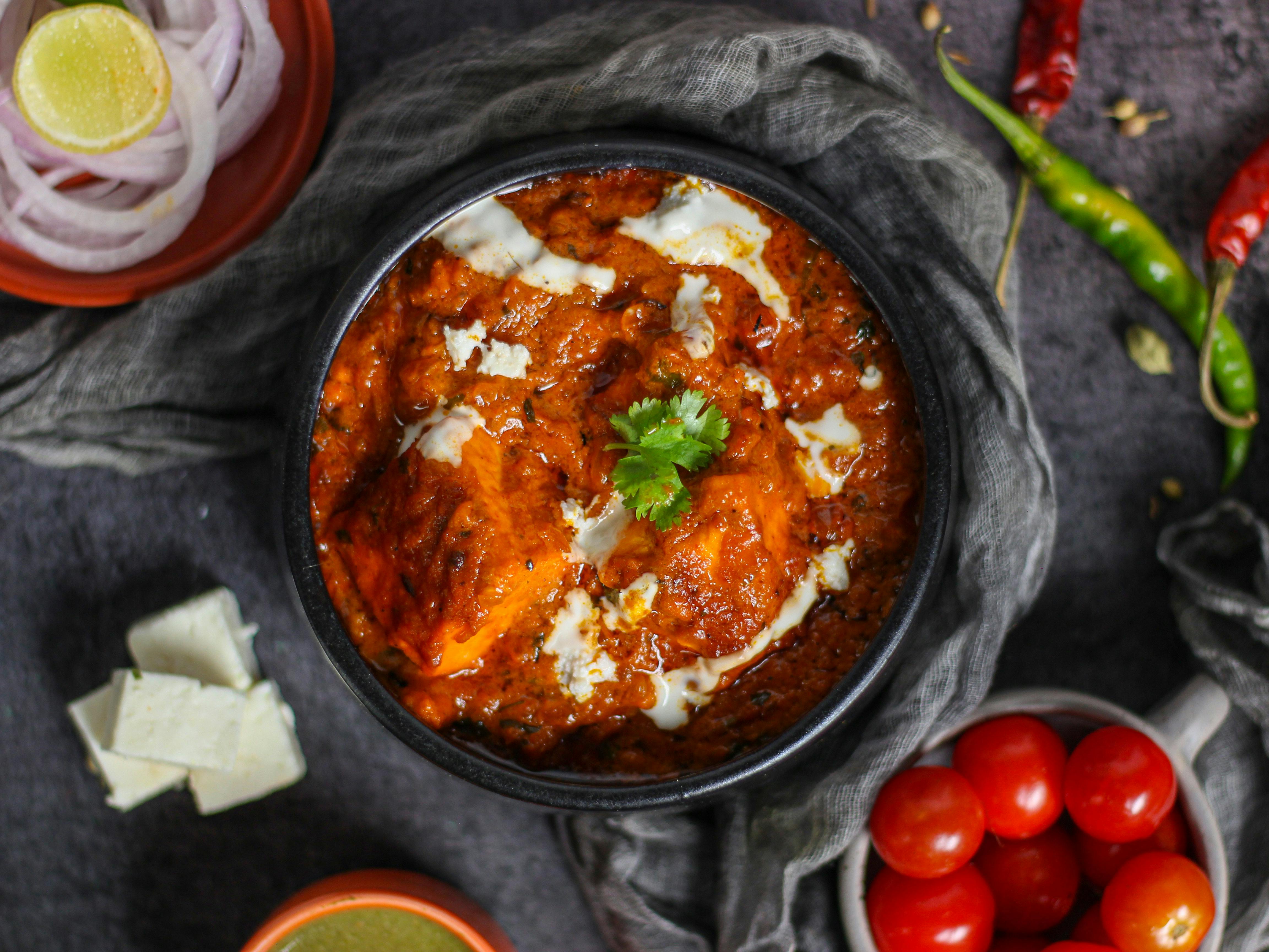 Paneer butter masala seen from above, surrounded by ingredients.